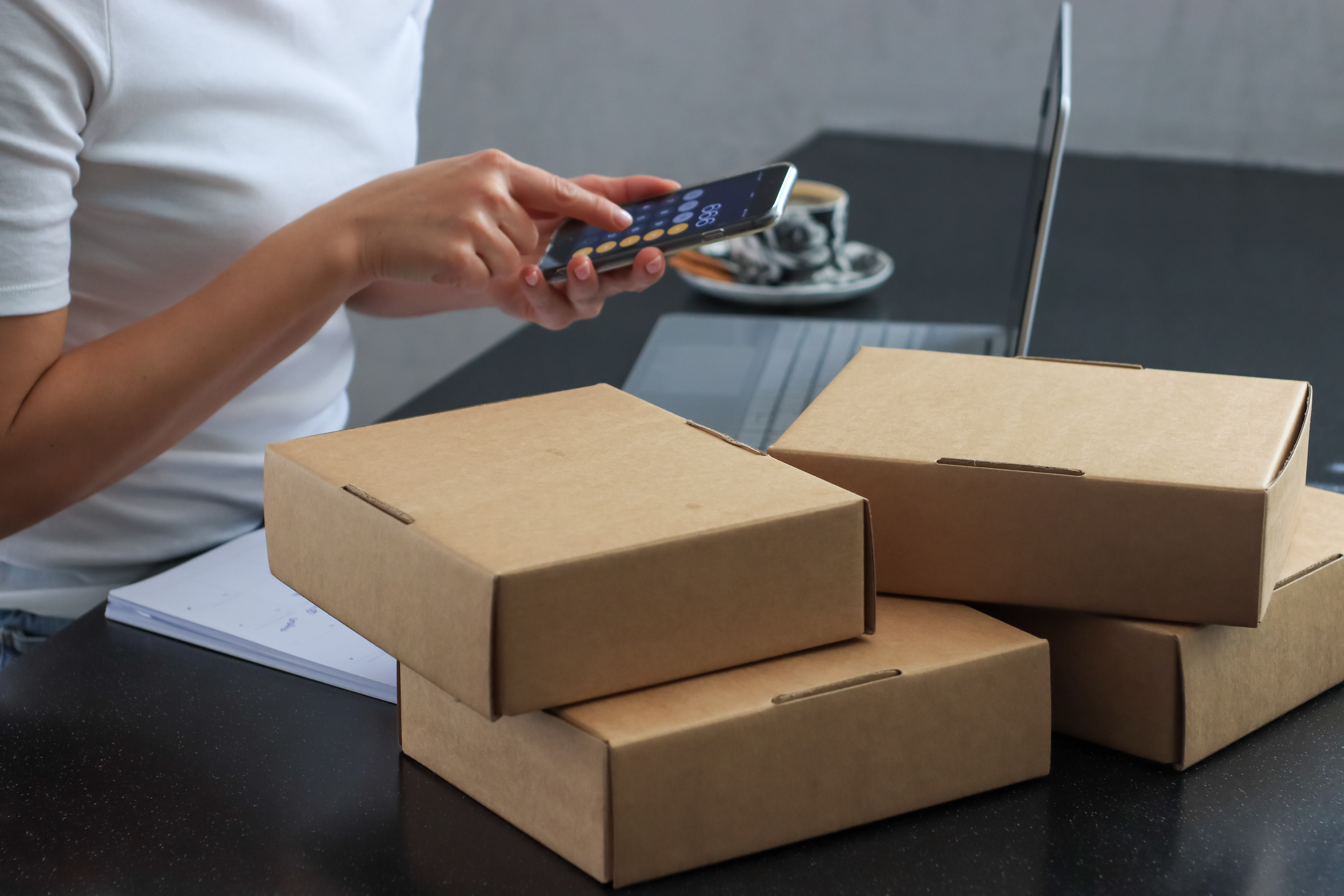woman calculating shipping costs on her phone next to a stack of packages