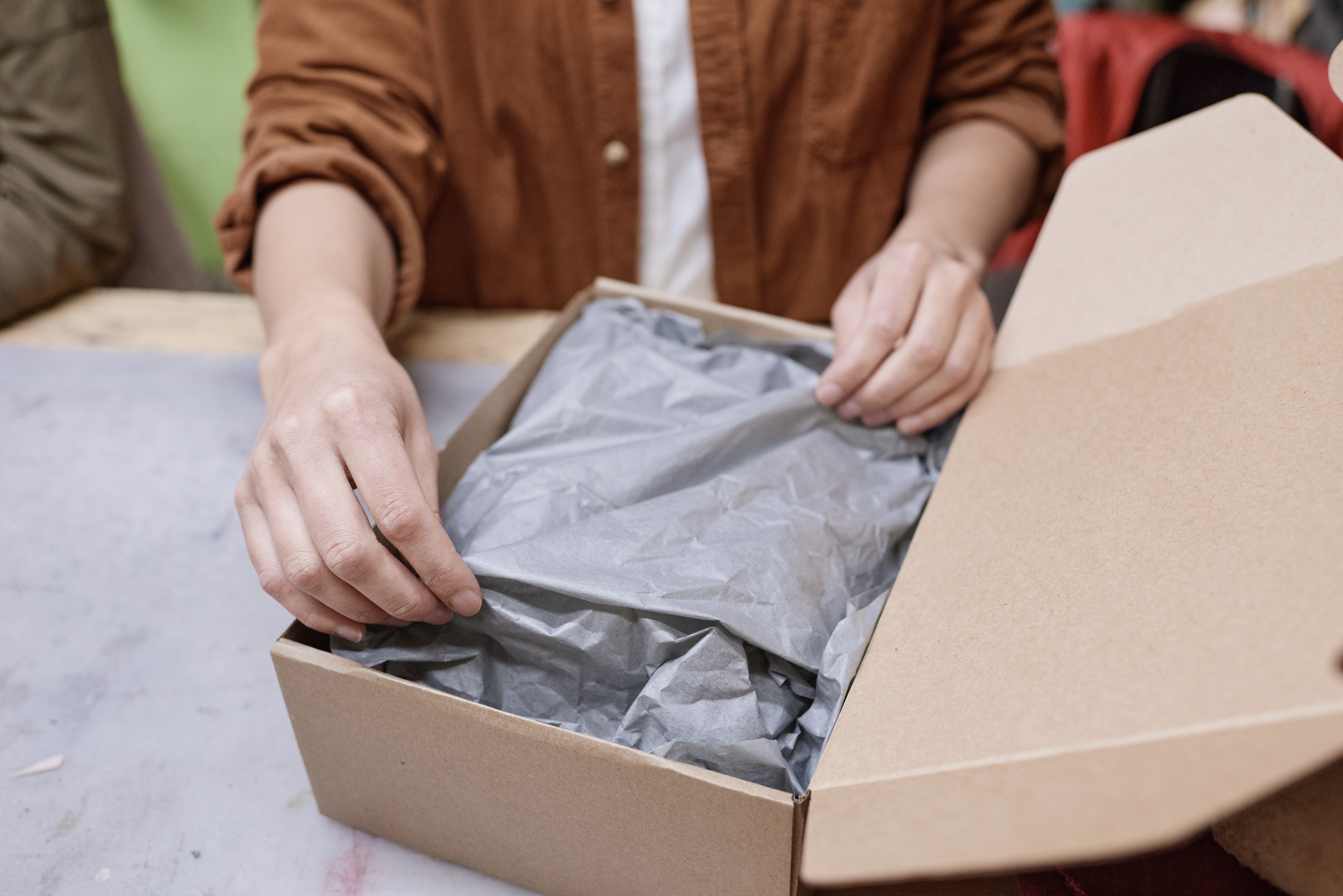 a man opening a brown cardboard box and removing gray tissue paper